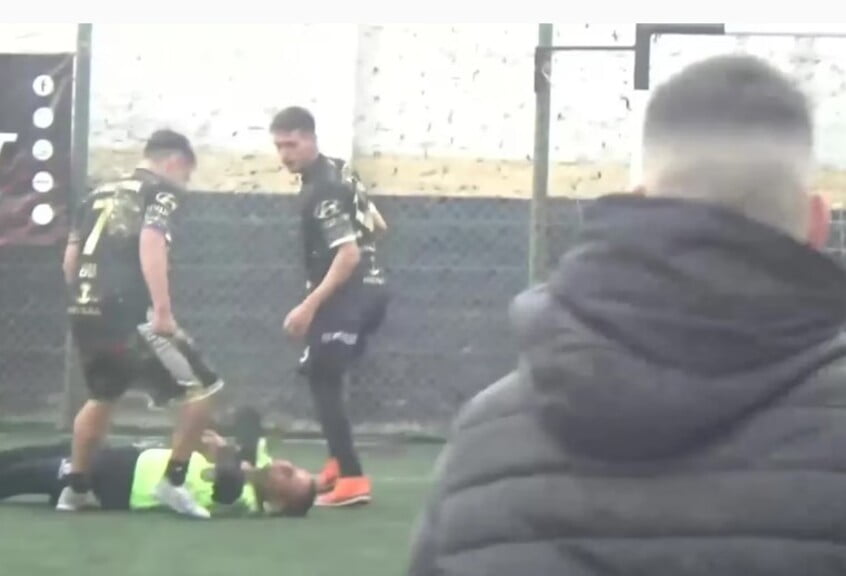 El momento de la caída del árbitro en el complejo de canchitas de Avellaneda, rodeado por dos de los agresores.